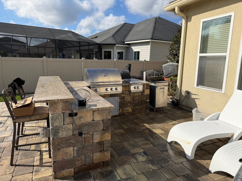 Backyard patio with stone outdoor kitchen, grill, bar seating, lounge chairs, and covered pergola area